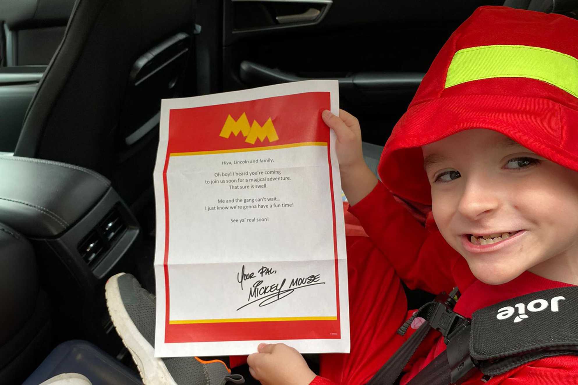 Lincoln sitting in a car seat, holding the letter he received from Mickey Mouse.