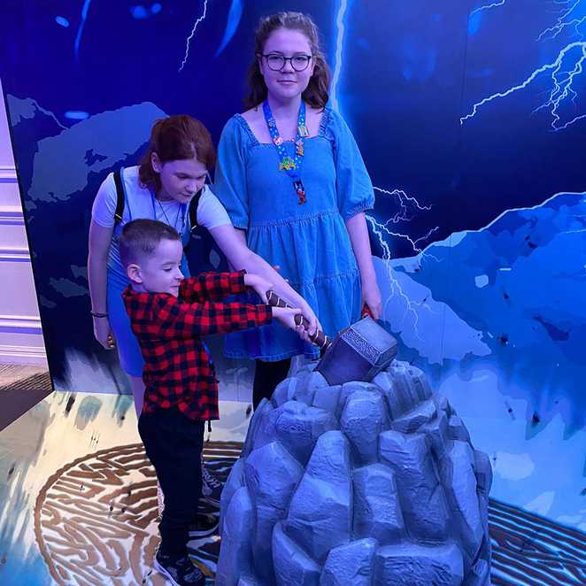 Lincoln's sisters helping him to try and lift Thor's hammer.